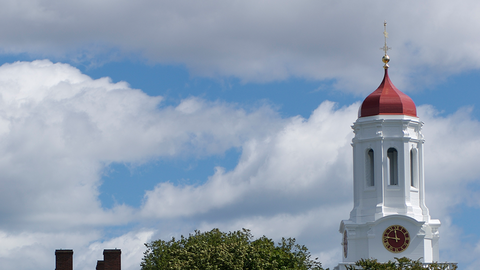 Top of a Harvard building against a cloudy blue sky.