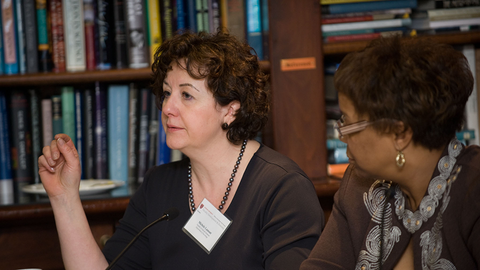 Two faculty members speaking on a panel with a bookshelf in the background.
