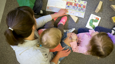 Caregiver reading a book to two young children.