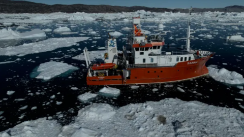 A red research vessel in icy waters in Greenland.
