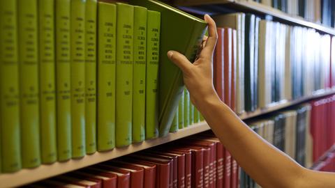 Closeup of a hand picking out a book from a bookshelf in a library.