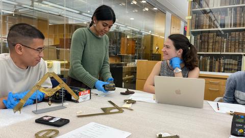 Students examining historical scientific instruments around a table.