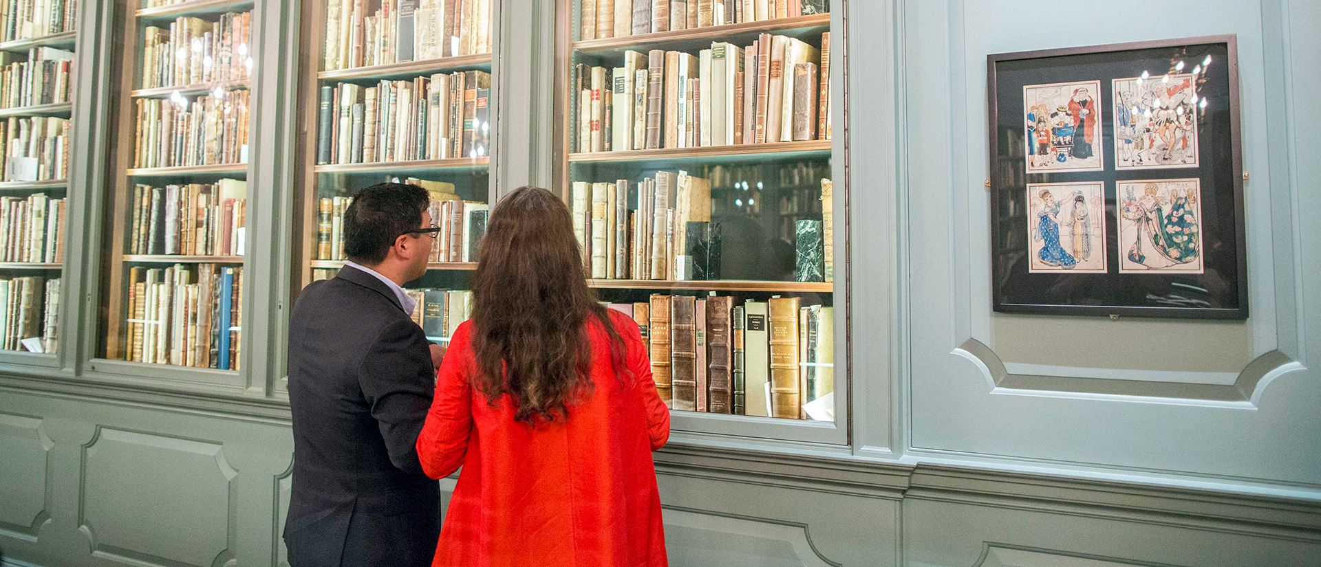 Two faculty members browsing rare books on the shelves of Houghton library.