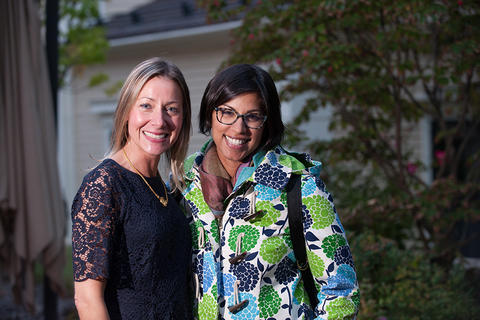 Two faculty members pose for the camera, smiling, in front of the Faculty Club.